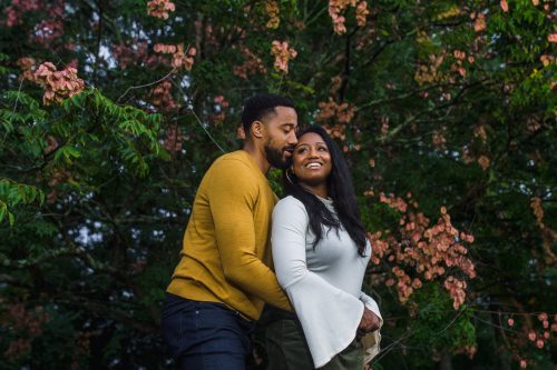 romantic engaged couple snuggled in front of peach-colored flowering tree at piedmont park