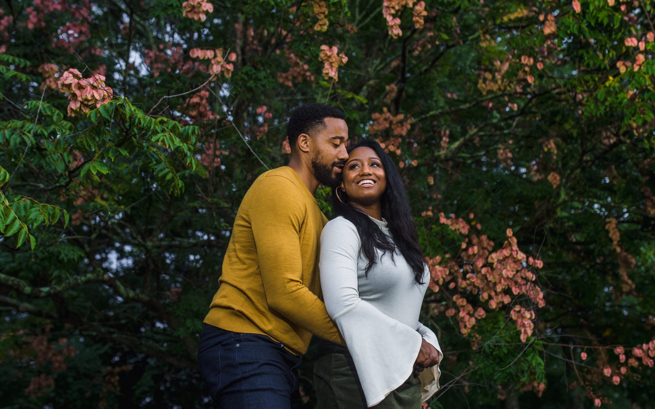 romantic engaged couple snuggled in front of peach-colored flowering tree at piedmont park