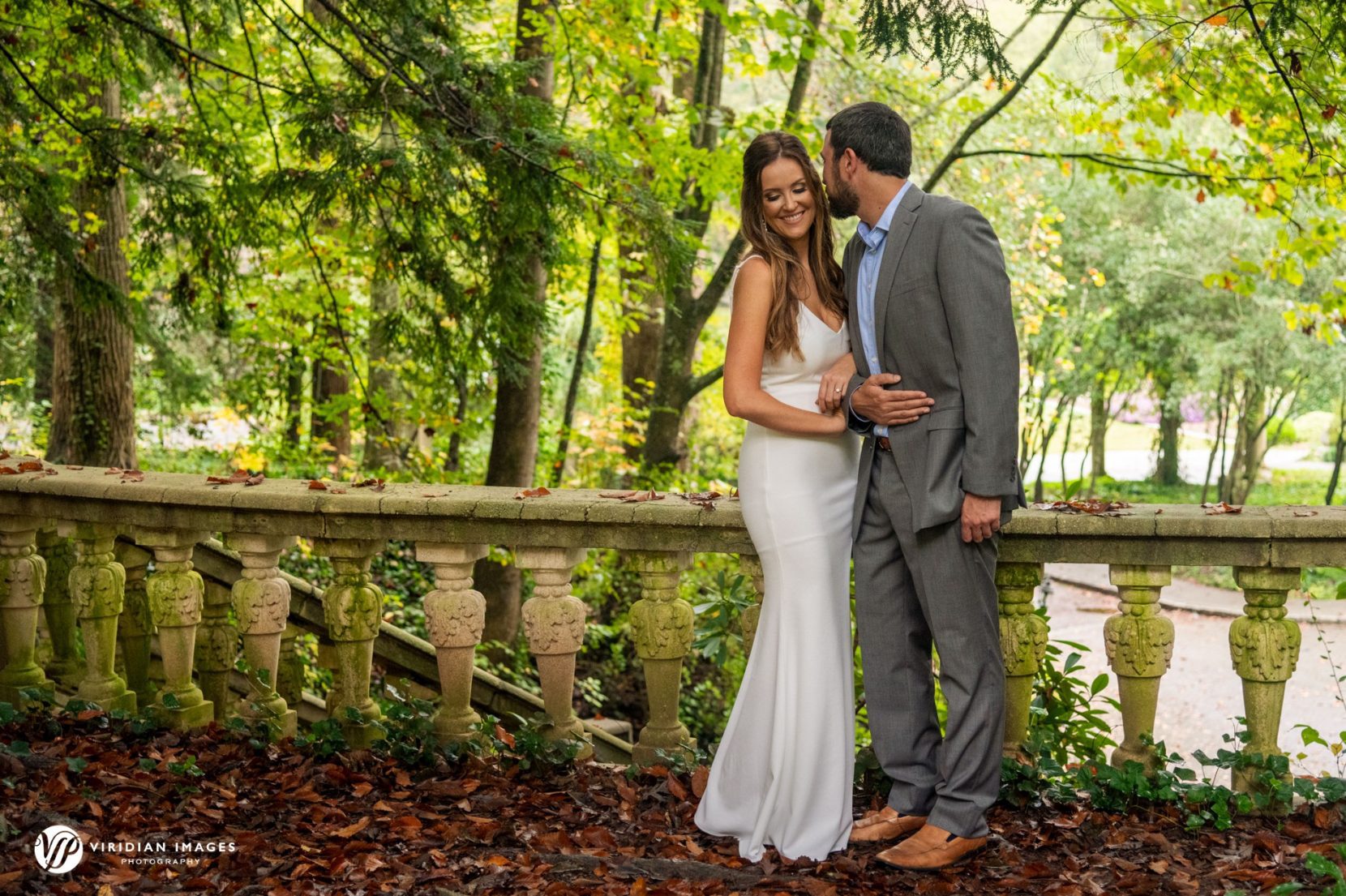 couple arm in arm and bashful kissing during engagement session in garden