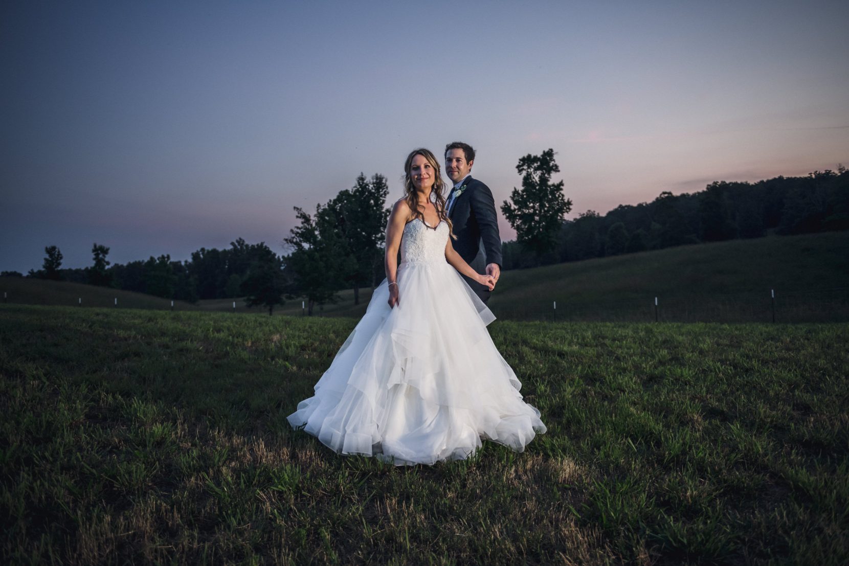Stylish wedding portrait of couple against a dramatic sunset on the hilltop at In The Woods, captured with an editorial, cinematic feel.