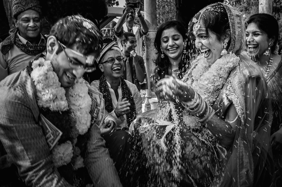 Southeast asian wedding ceremony throwing rice and laughing as family look on.