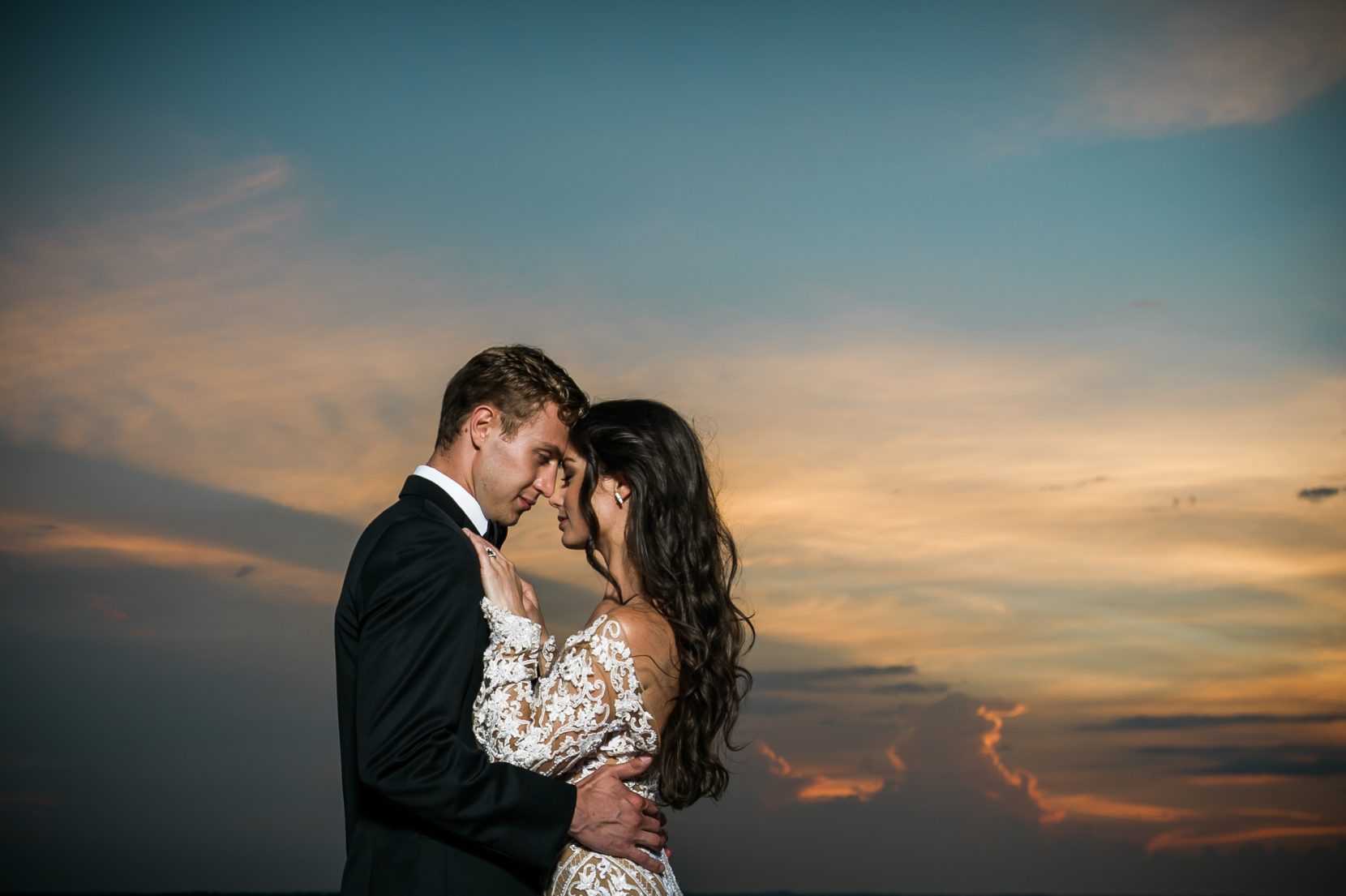 Romantic wedding photo of couple holding each other on the Ventanas helipad, framed by the glow of the setting sun over Atlanta.