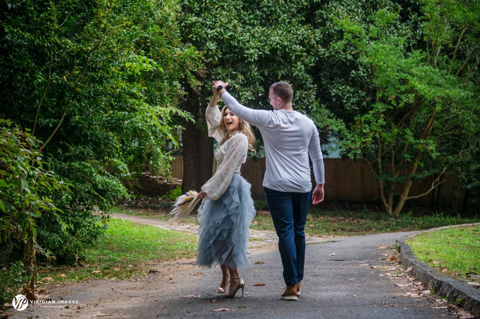 engaged couple spinning along tree-lined path in Atlanta