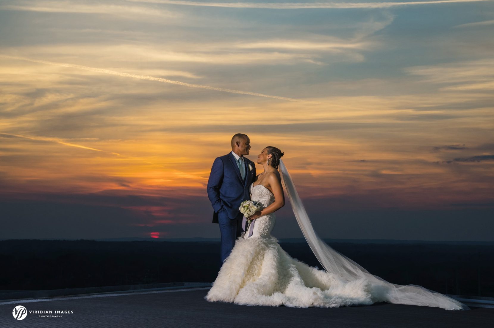 bride and groom looking at each other against sunset on top of Ventanas rooftop helipad