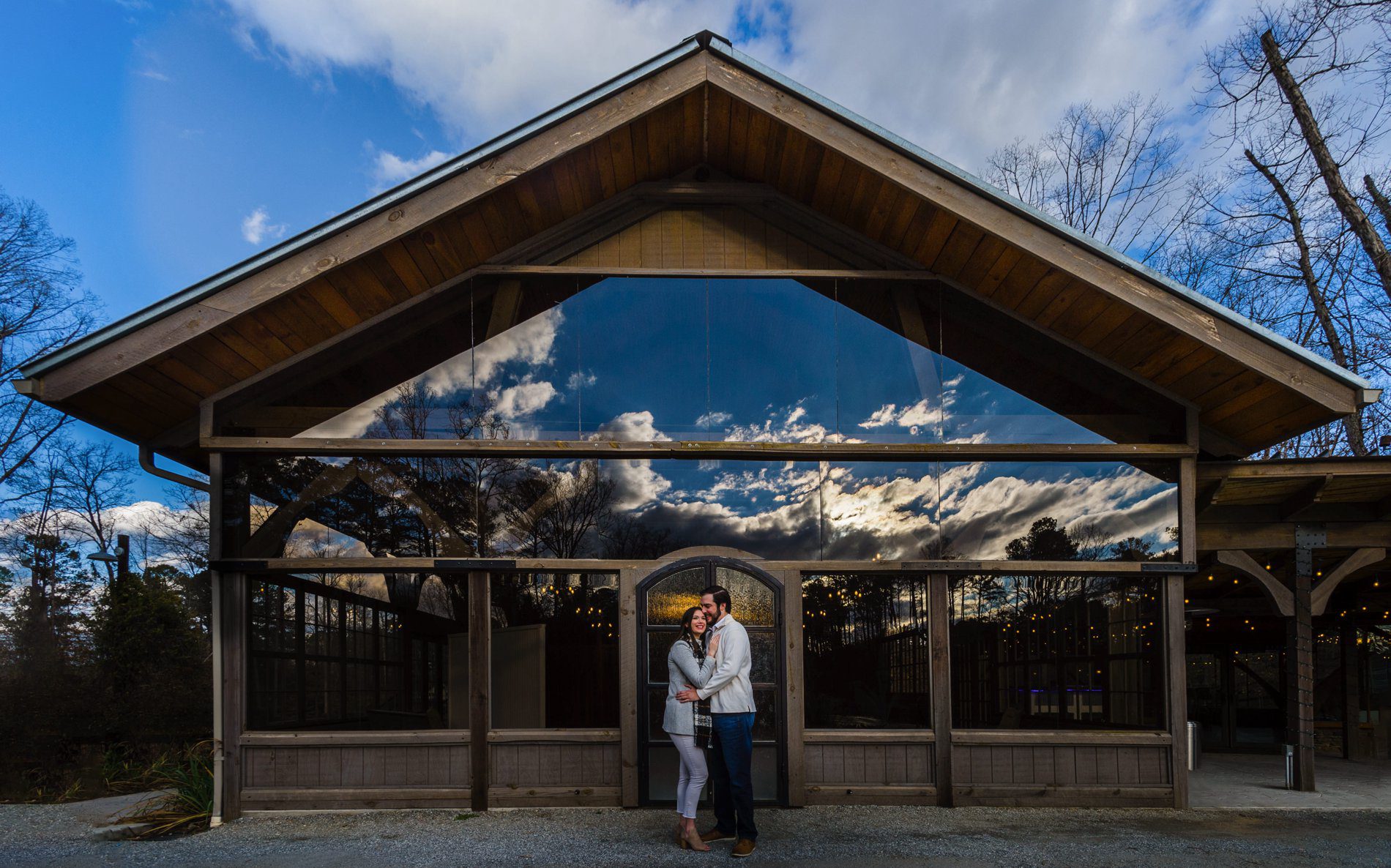 Engagement photo of couple standing in front of reflective windows showing a dramatic sky at Rocky Lake Estate.