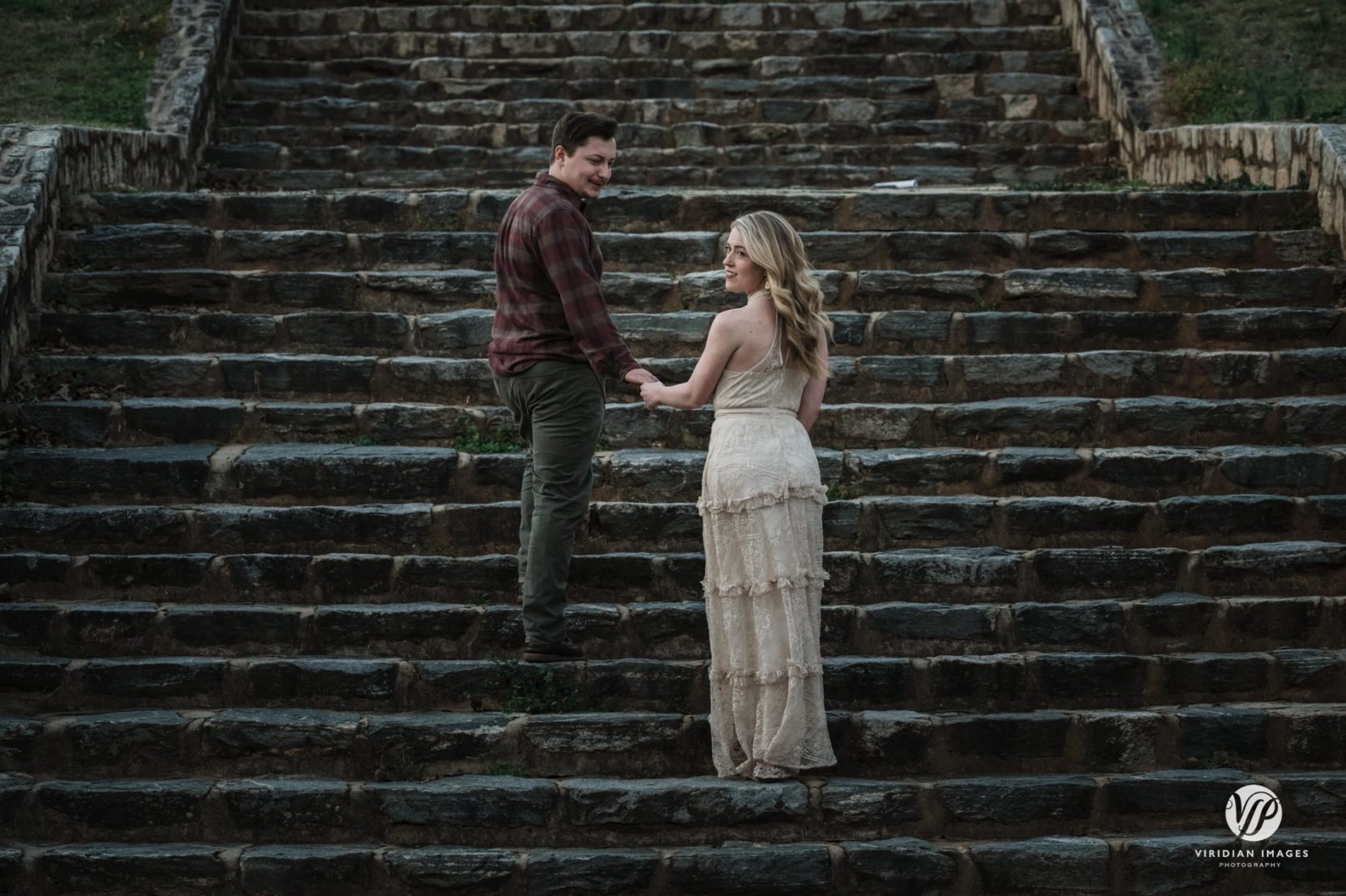 Groom wearing burgundy plaid shirt and green slacks helping bride up stone staircase in Piedmont Park