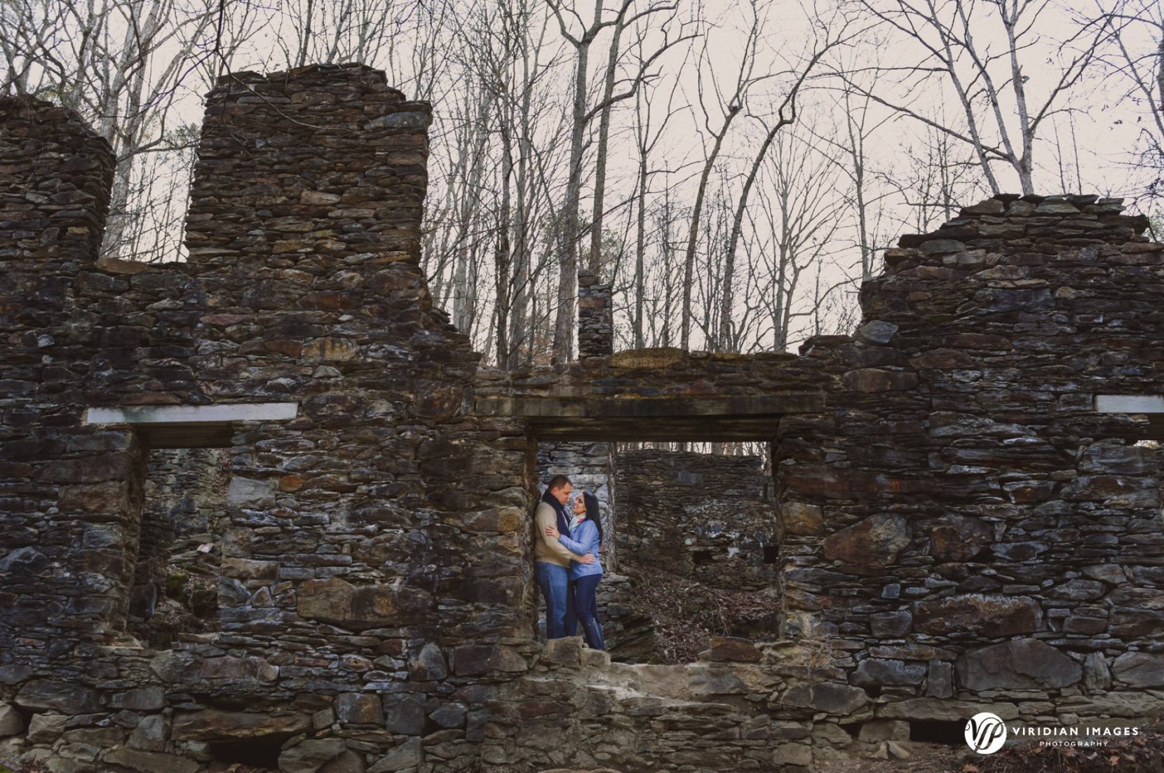 Wide shot of couple through window frame of old ruins during engagement session at Sope Creek Trail
