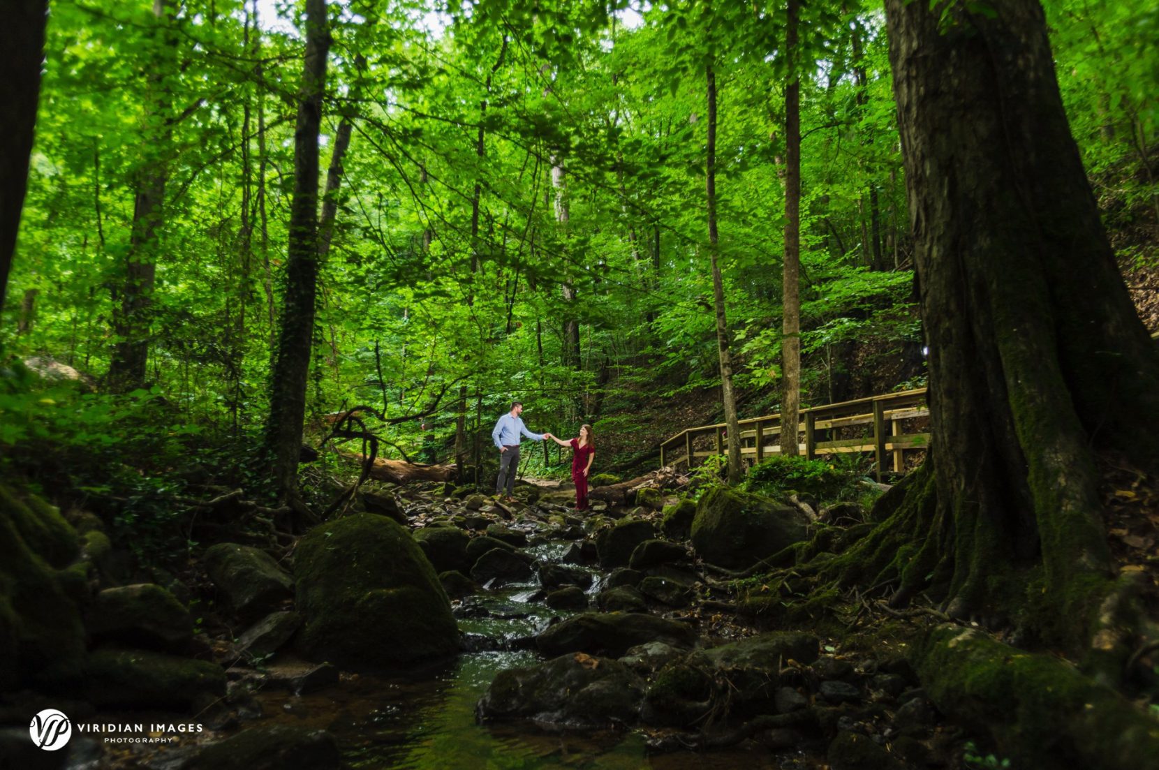 Engaged couple holding hands over creek at Cascade Springs park