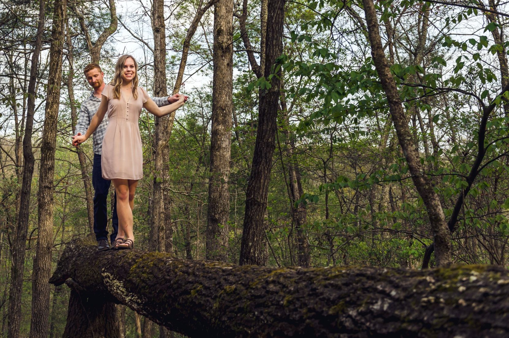 Lower angle of couple balancing on fallen tree during engagement session