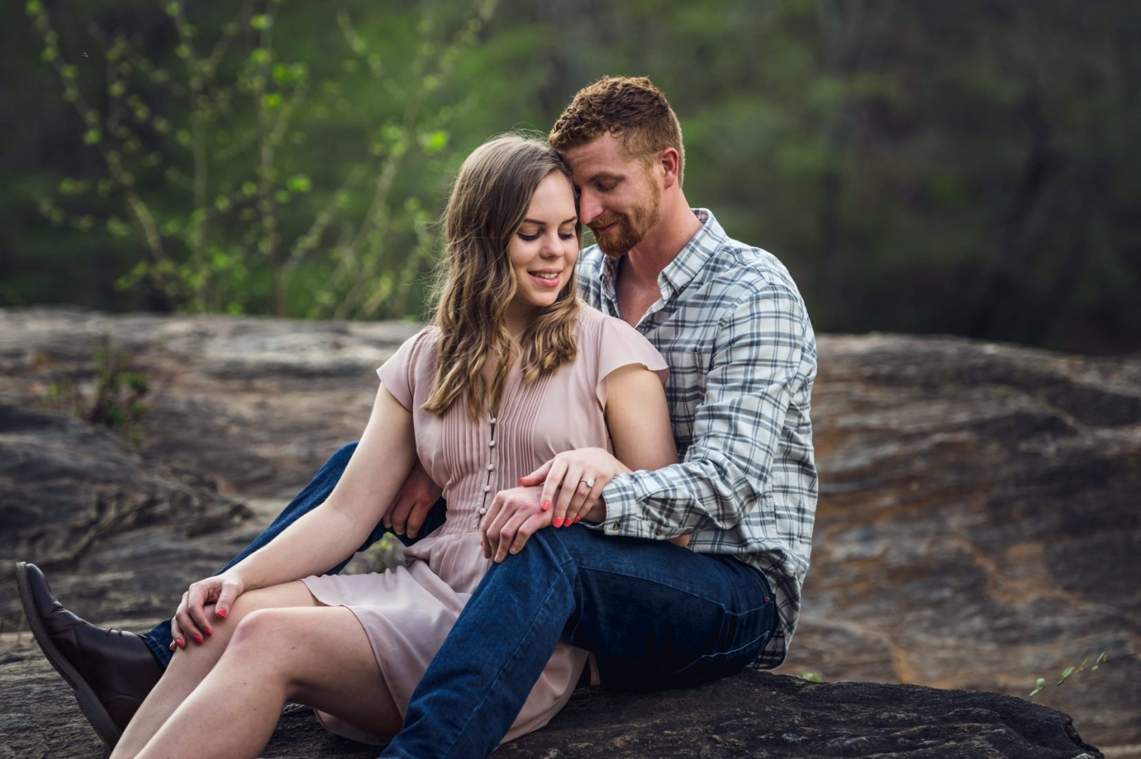 Couple sit on rock by the river edge during engagement session at Sweetwater Creek