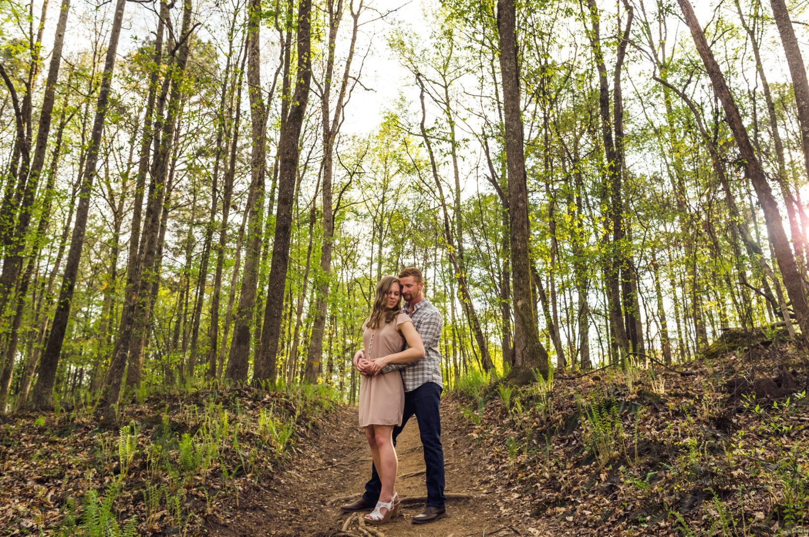 Romantic moment of couple together between spring leaved trees at Sweetwater Park engagement session