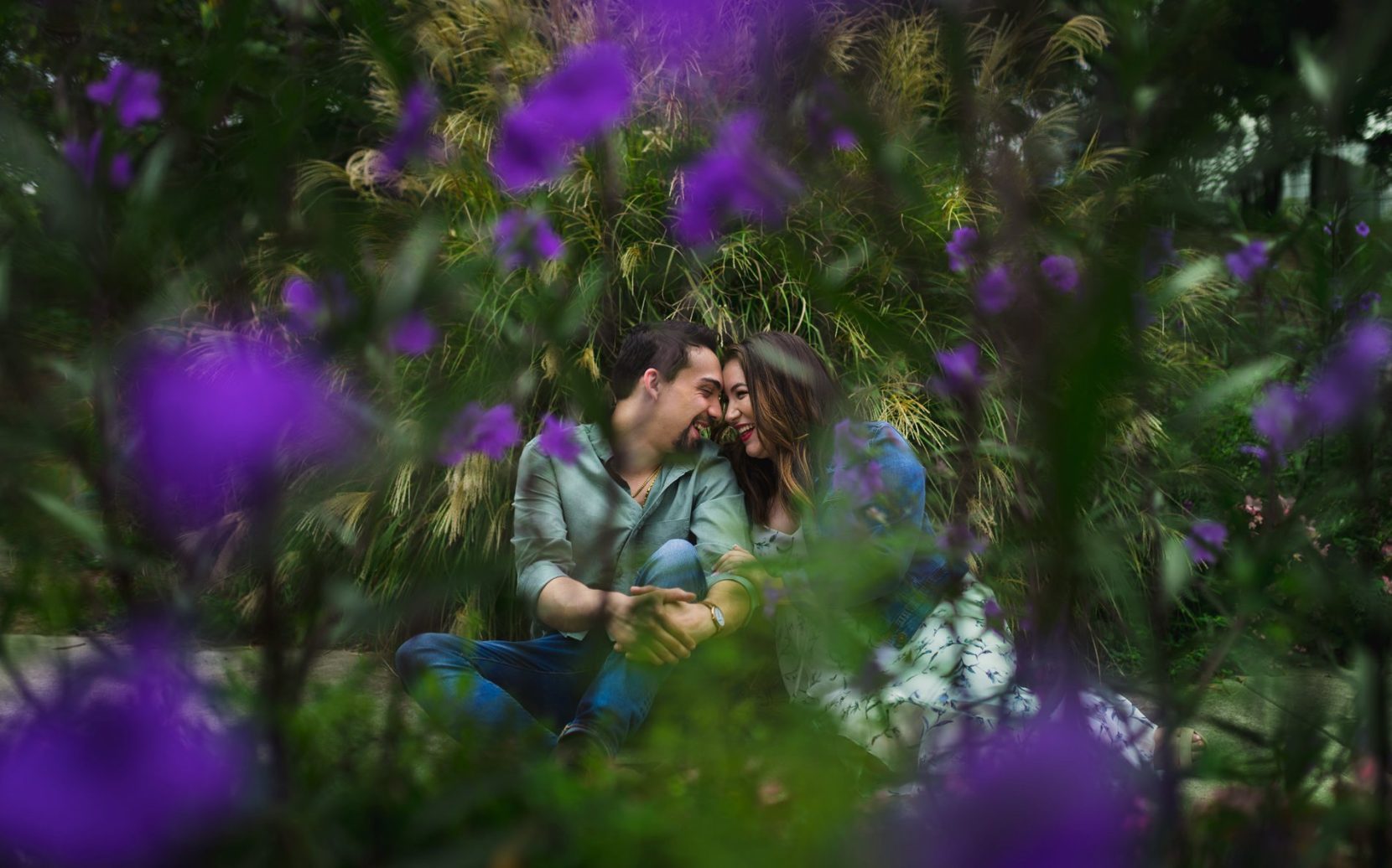 Couple sitting together and laughing between flowers during engagement session at Piedmont Park, Atlanta