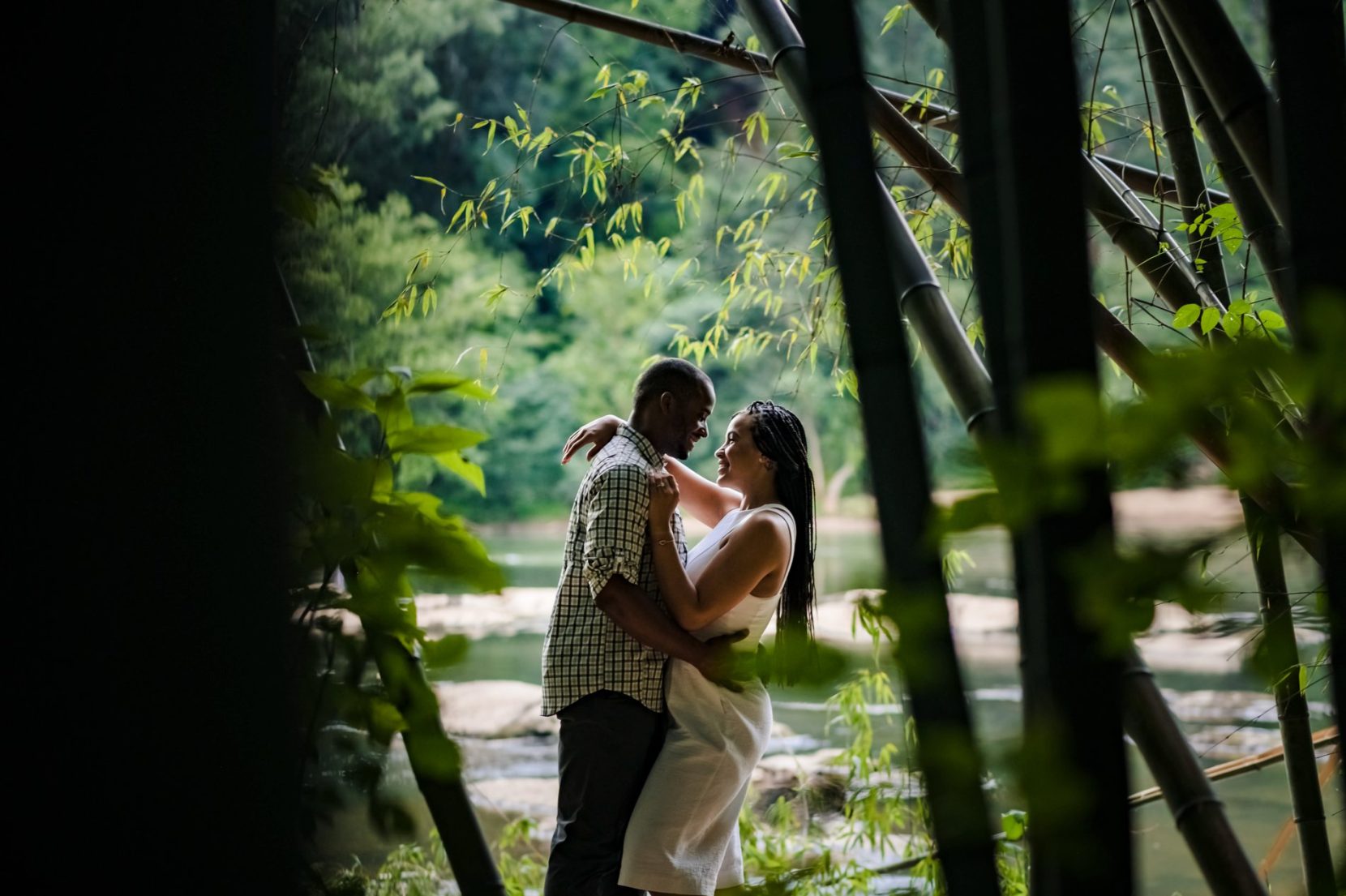 Couple face to face between bamboo trees and river background during engagement session on Chattahoochee River