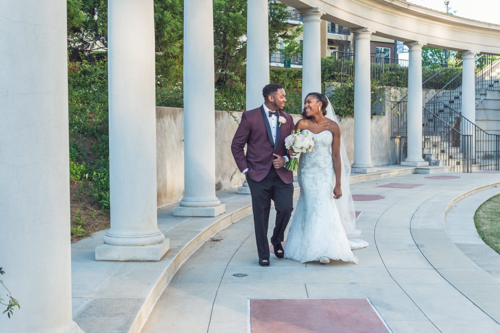 Couple walking through a column-lined architectural walkway at a formal wedding venue
