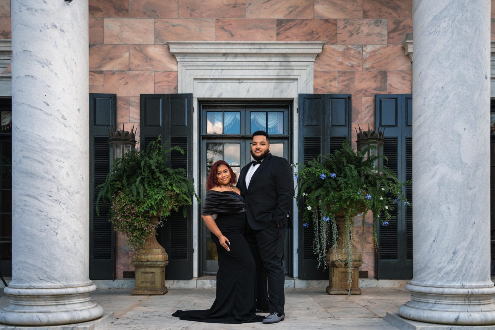 Close portrait of a couple in front of a classic estate home with architectural framing