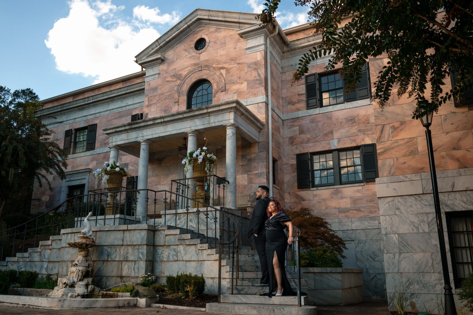 Couple posed on a curved staircase within a formal estate setting