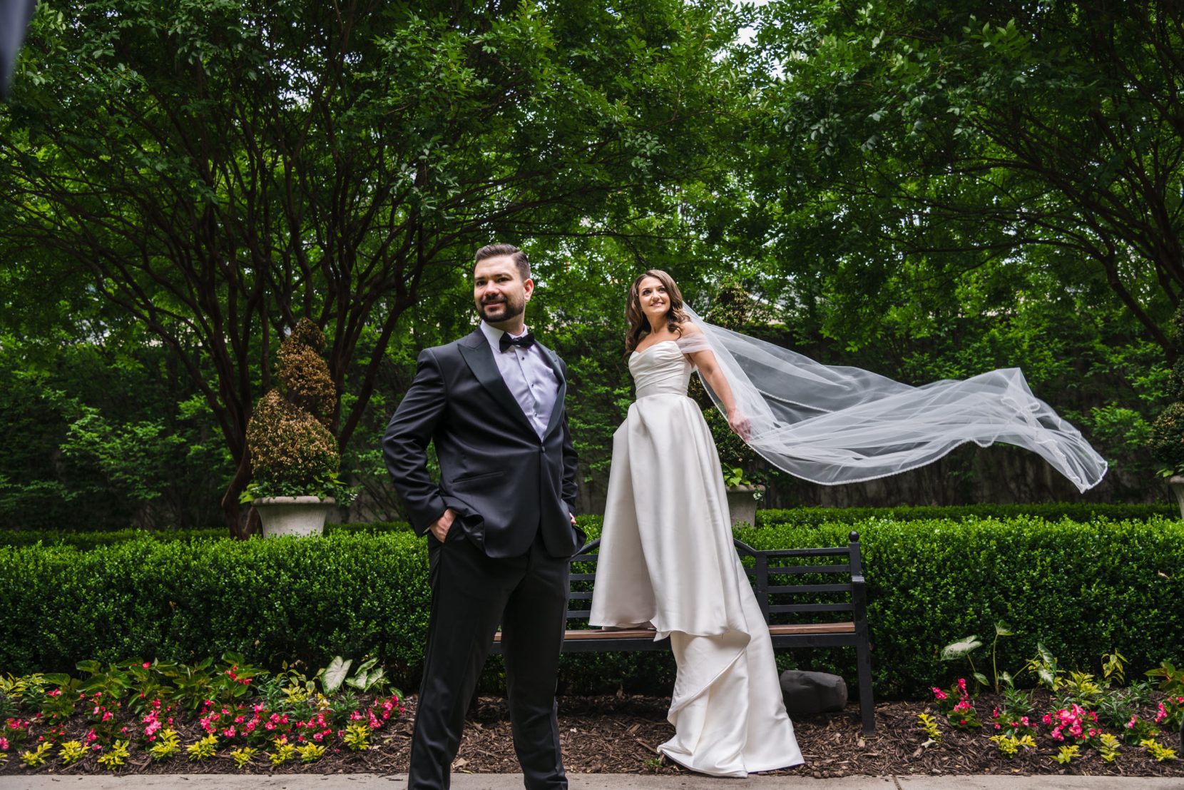 Editorial-style couple portrait in a formal garden with soft movement and greenery